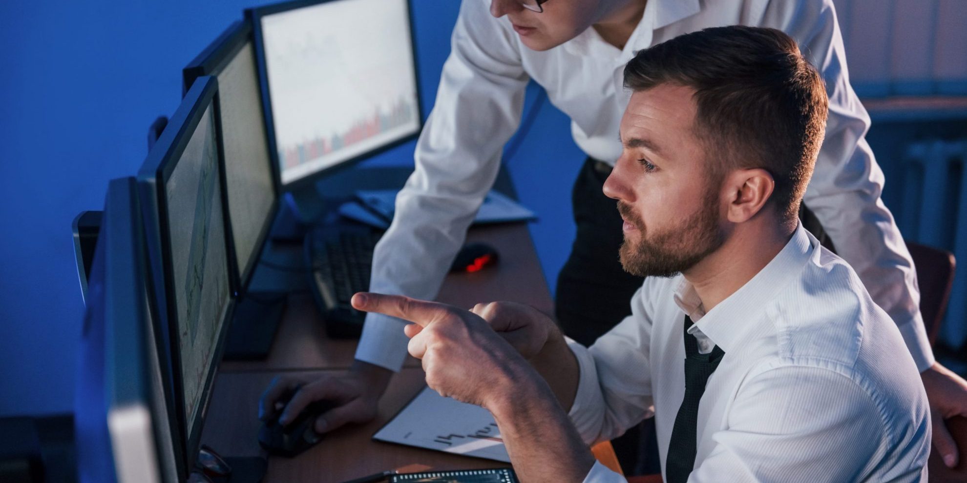 Photo of two men looking at computer screens illustrates blog "CMMC Continuous Monitoring: What Is It and Why Is It Important?"