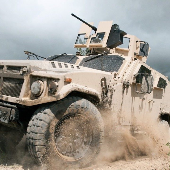 Military light armored vehicle going up a dirt road with trees in the background.