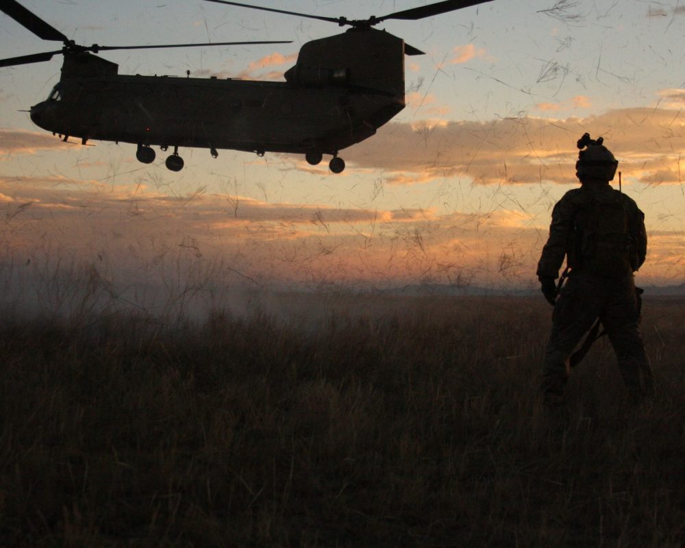 Military transport helicotper against sunset with person in the foreground.